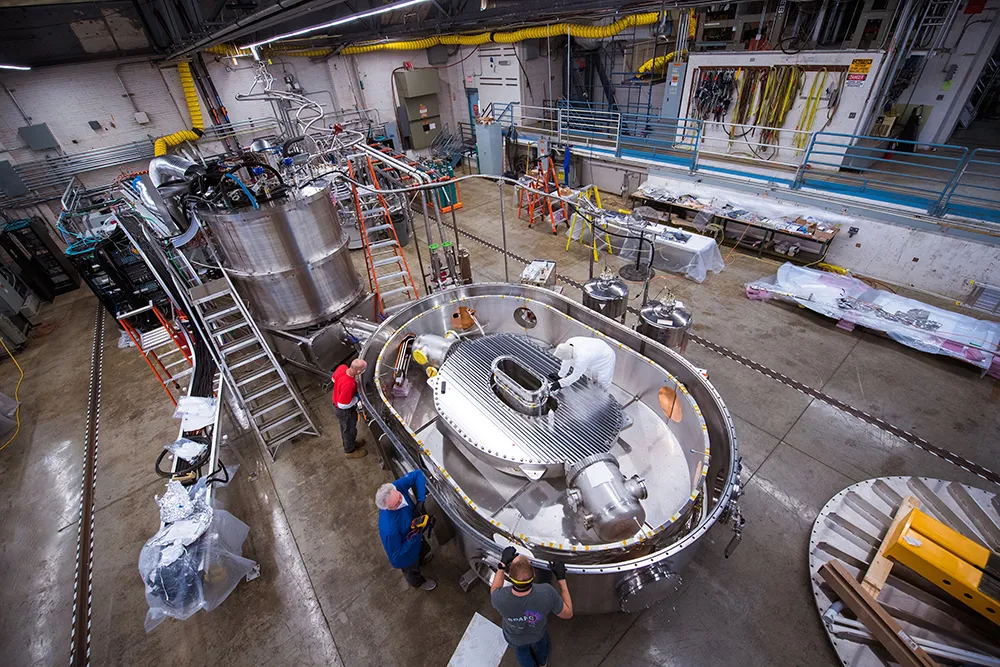 Large-bore, full-scale high-temperature superconducting magnet in a building with researchers working on it.