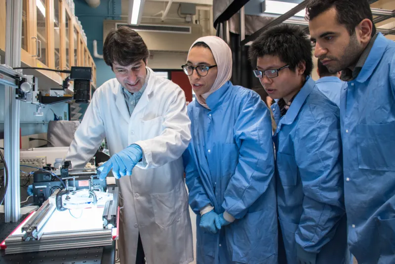 Professor and students review experiment under a microscope.