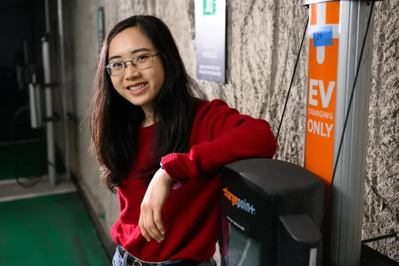 MIT senior Elaine Siyu leans against an EV chargepoint. 