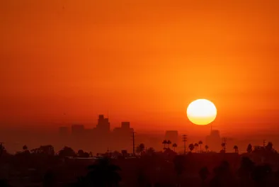 A bright sun hangs just above a city against a deep orange sky